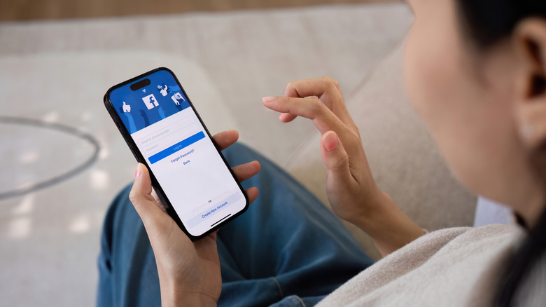 Woman holding a phone showing the Facebook log in page