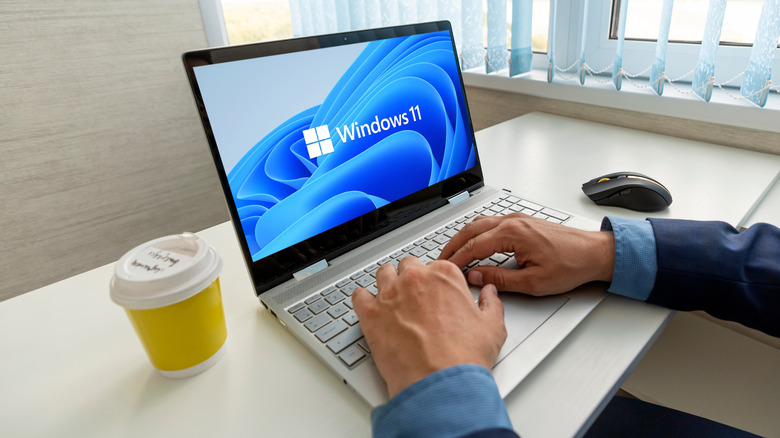 Man working at office on a laptop showing Windows 11 logo and wallpaper