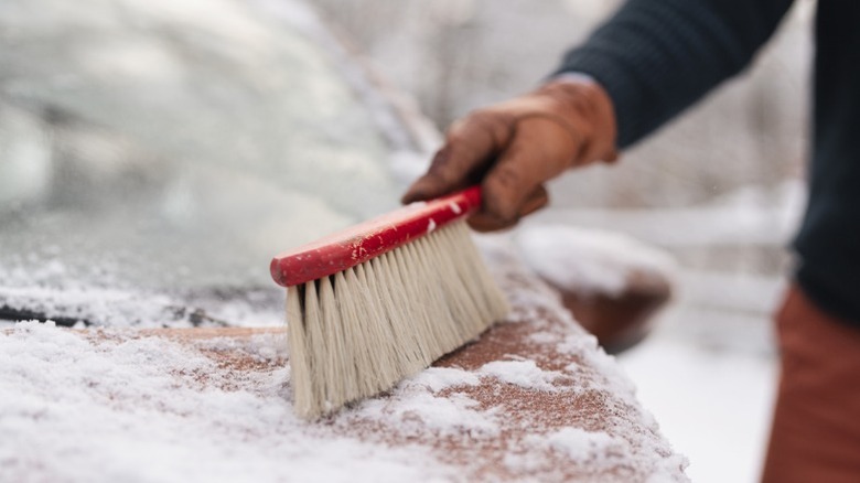 A person using a small hand broom to remove snow from their car