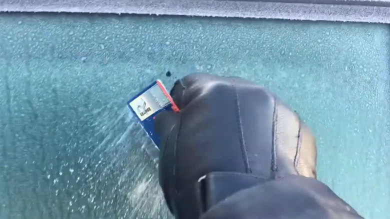 A person using an old credit card to scrape ice off their car windows