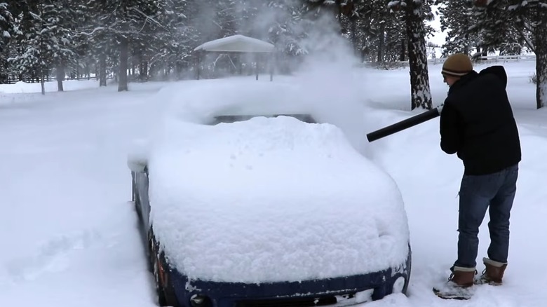 A person using a leaf blower to remove snow from their car