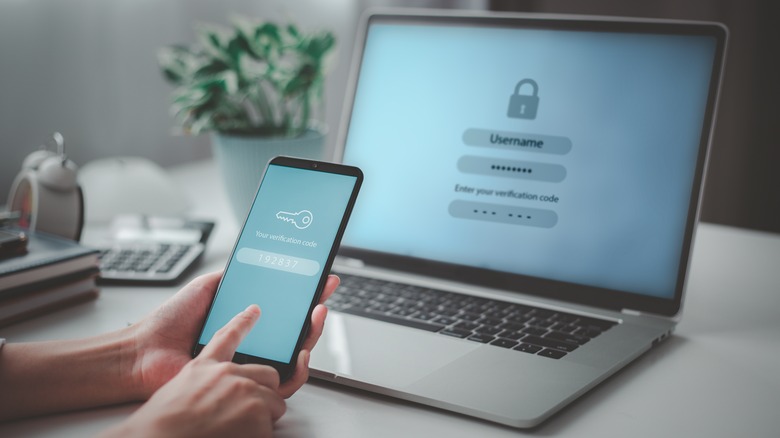 Smartphone with passcode on screen in front of laptop displaying user login screen