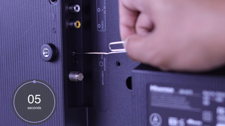 Hand inserting pin in reset button on Hisense TV