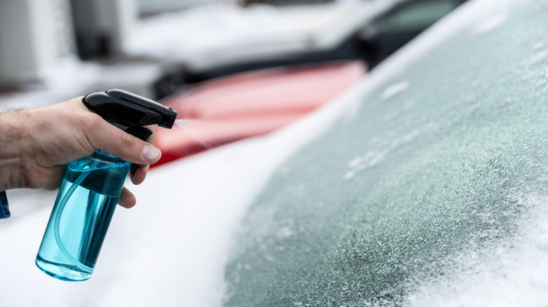 Man uses a bottle of de-icer to defrost the ice-covered windshield