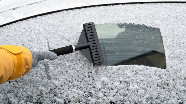 Driver is removing snow from car windshield with ice scraper