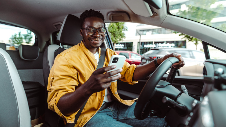 person in car smiling at smartphone