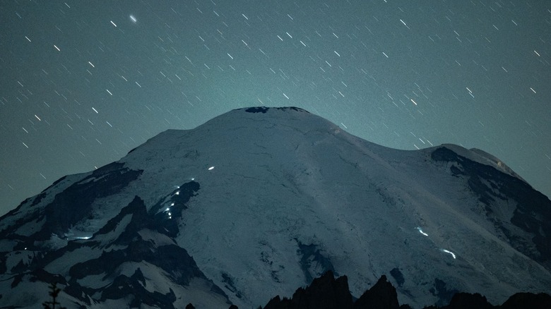 Mt. Rainier underneath a star filled sky with the lights of climbers making their way to the summit.