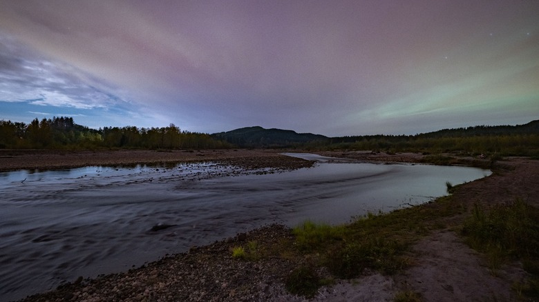 Long exposure photo of a river and cloudy night sky lit by the aurora borealis.