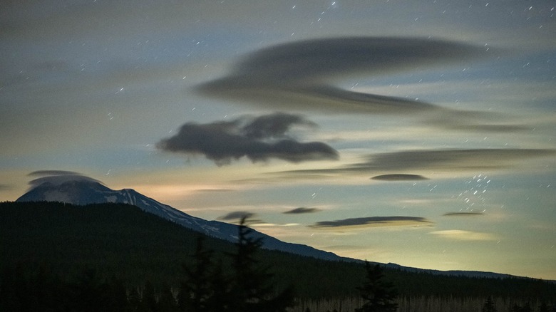 Mountains with lenticular clouds swirling beneath a sky full of stars.