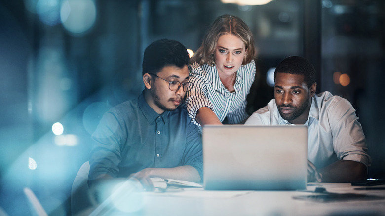 Three people using a laptop