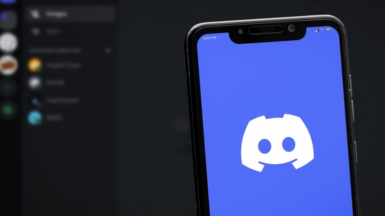 Discord on mobile phone with the app on a laptop in the background