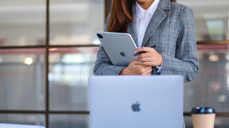 person holding iPad in front of laptop