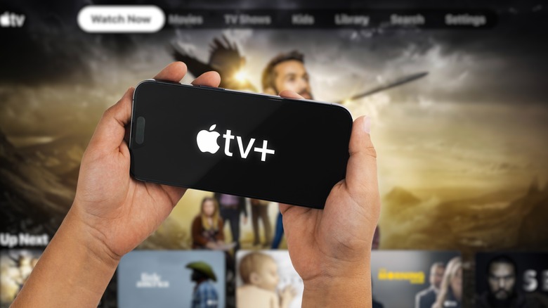 An iPhone with Apple TV+ logo on its screen in front of a TV