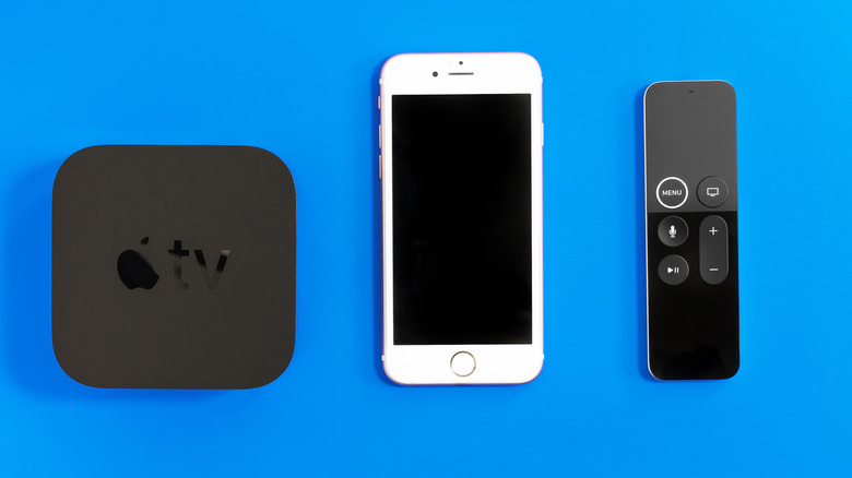 An iPhone in between an Apple TV device and a remote control