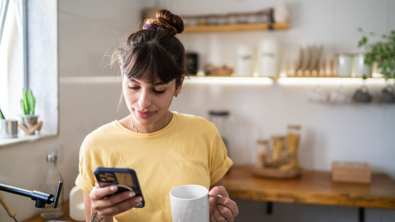 woman with mug using iPhone