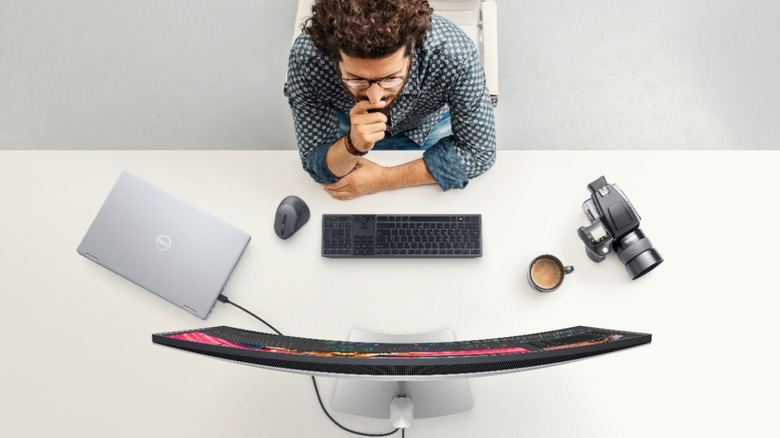 Man working on a closed laptop connected to a curved monitor on a table