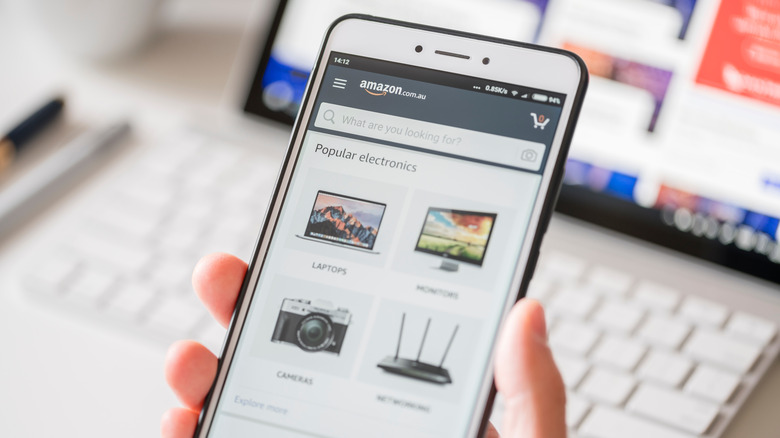 A hand holding a white smartphone with the Amazon shopping app open.