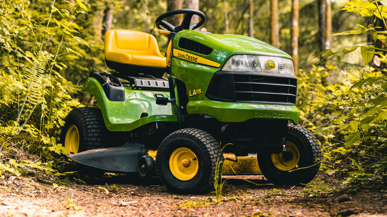 A riding John Deere lawn mower parked in the woods