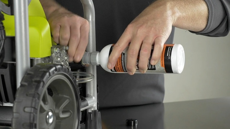 A hand holding a bottle of pump protector up to a Ryobi pressure washer.