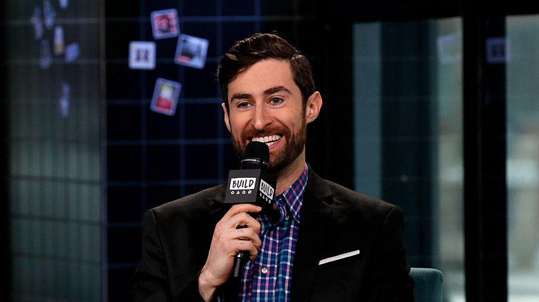 Scott Rogowsky speaking into a microphone on TV