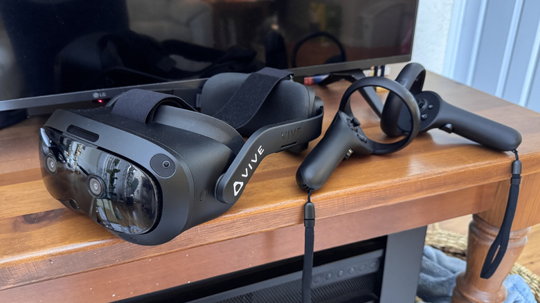 The HTC Vive Focus Vision with controllers in front of a television on a wooden table.