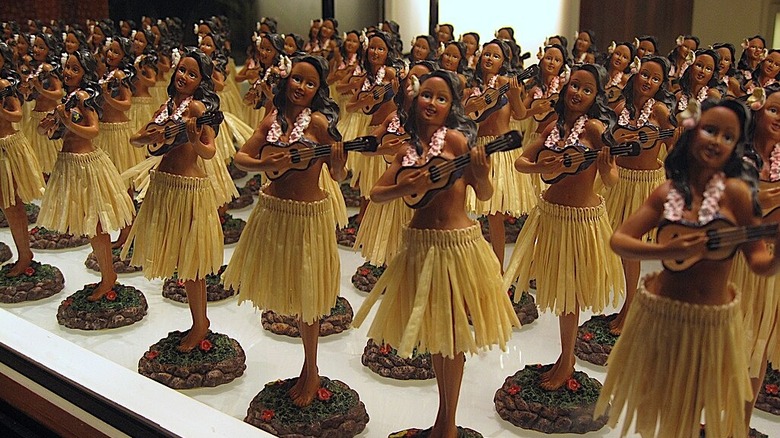 Dozens of colorful hula girl dolls lined up on a shelf for sale in a store.