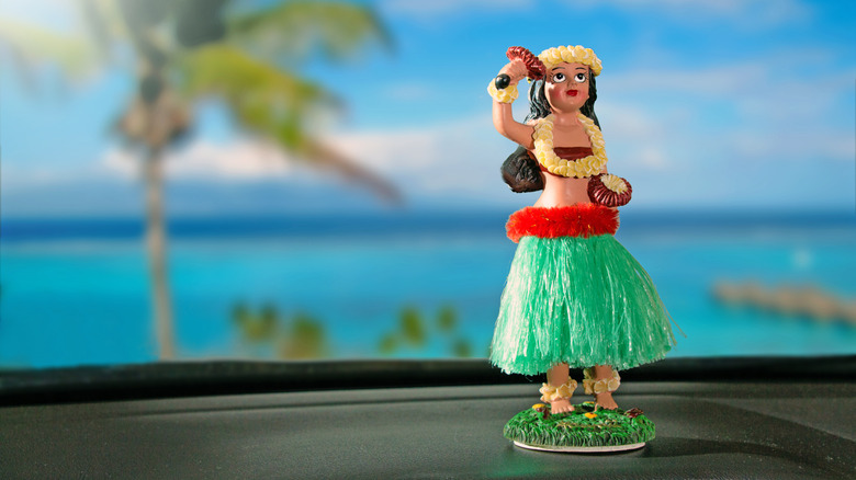 Hula dancer doll on dashboard car. The car is parking in front of the ocean.