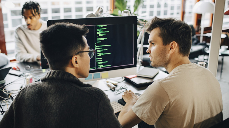 Two people sitting at a computer with code on the screen