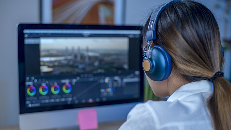 Woman editing video while wearing blue headphones