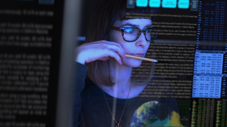 woman looking at a transparent screen with a pencil near her mouth