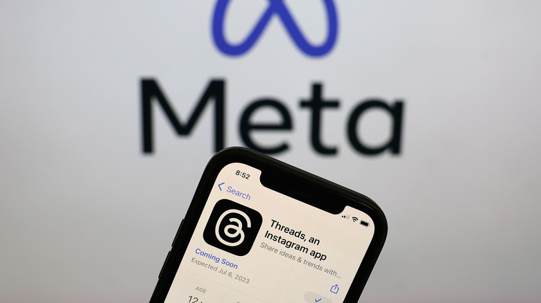 phone displaying Threads app in app store with Meta logo in background