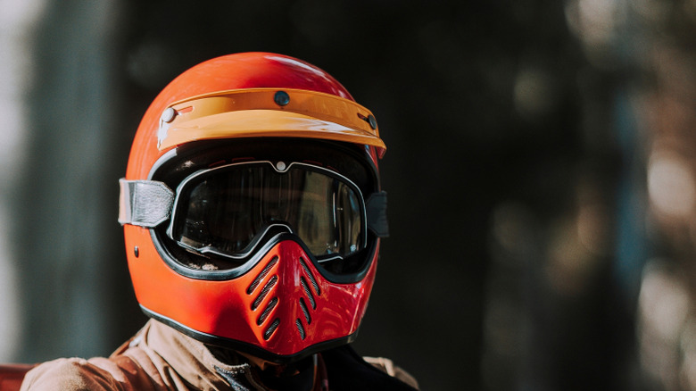 A person wearing a red and orange dirt bike helmet.