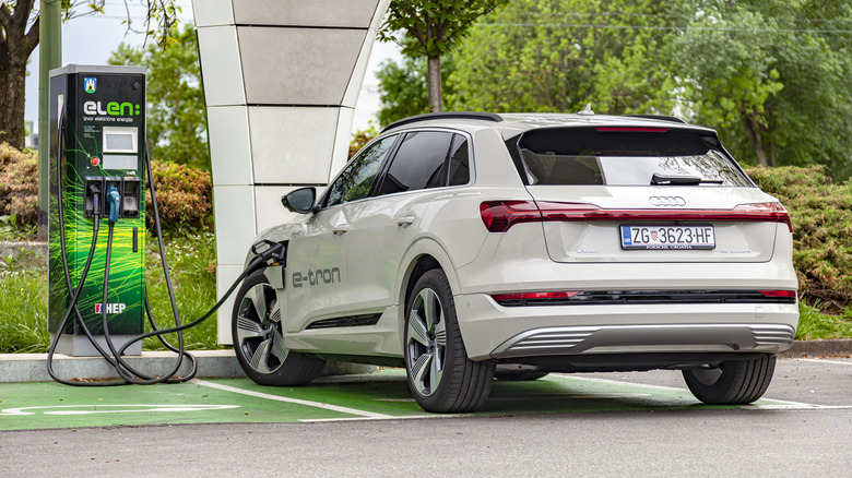 A white Audi e-tron replenishing its battery at a charging station