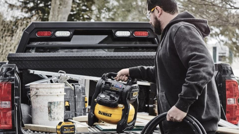 Contractor putting a DeWalt 2.5-Gallon 140 psi 20V Cordless Air Compressor﻿ in the back of a pickup truck