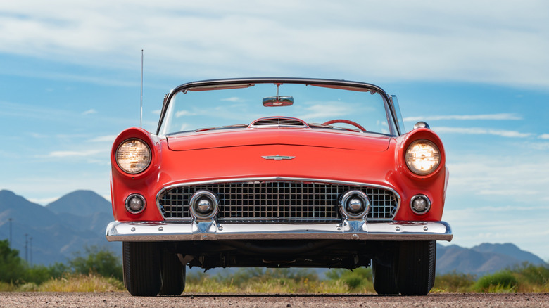 Red Ford Thunderbird convertible parked on dirt under a cloudy sky