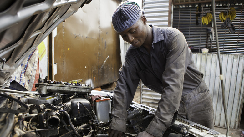 Young man in coveralls and knit cap working on car engine