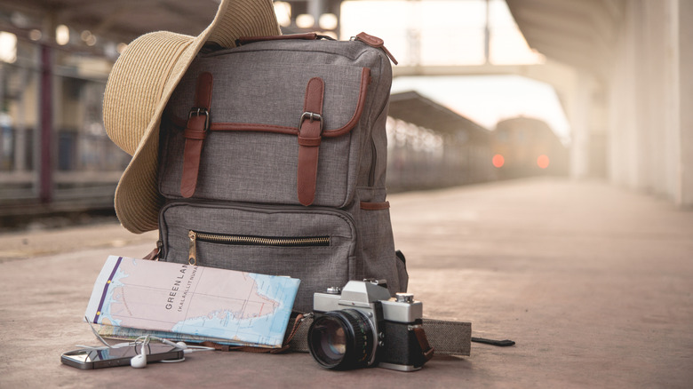 Vintage camera with film sits with a backpack and map at a train station, ready for exploring