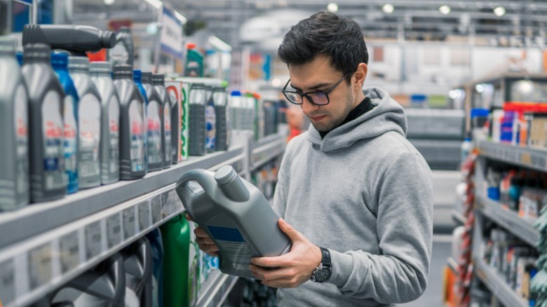 A person in an auto parts store holding and looking at a jug of motor oil