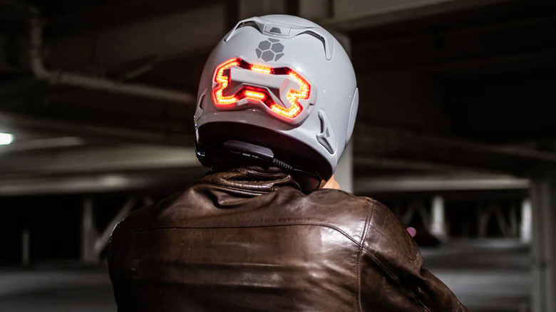 A rider in a brown leather jacket wears a white Brake Free helmet with the red light in back lit