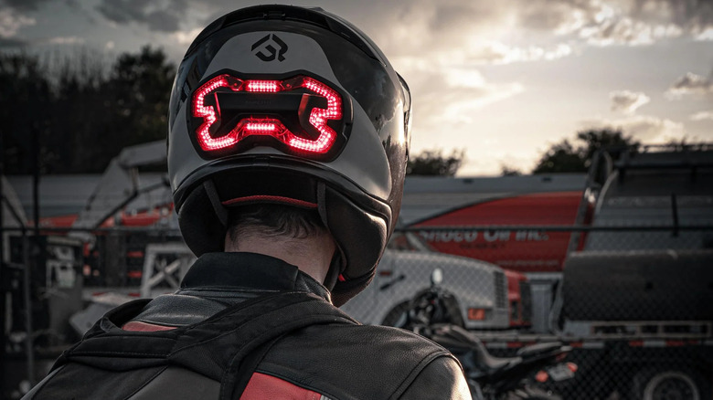 A rider in a black and red jacket and backpack with a Brake Free helmet light at a racetrack