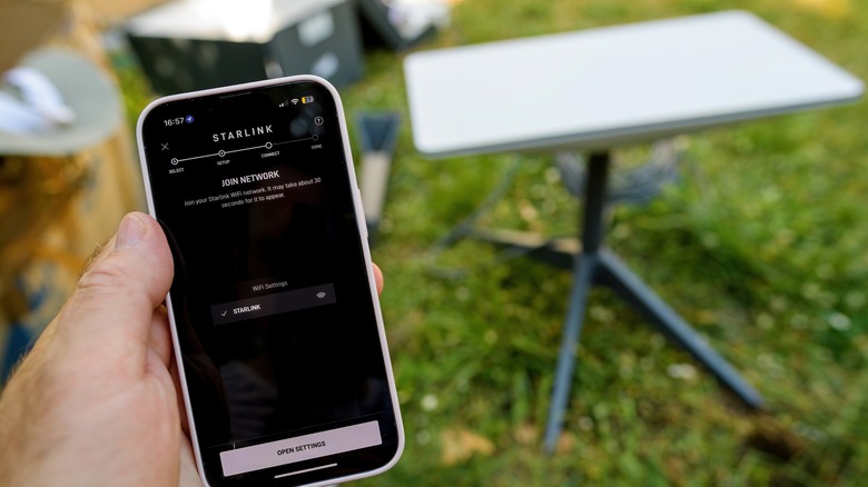 Starlink dish out of focus in background while Starlink's app is loaded on phone in foreground