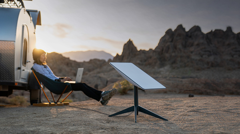 Starlink dish on the ground with woman working on her laptop in the background