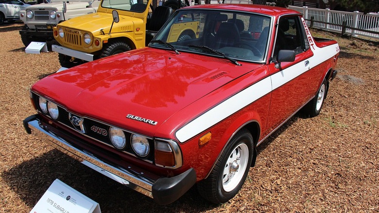 Red and white 1978 Subaru Brat parked on wood chips at car show