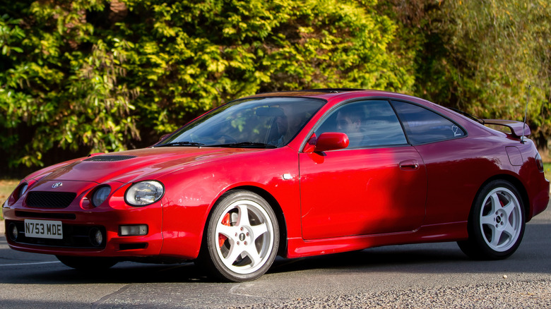 A red Toyota Celica driving on a paved road.