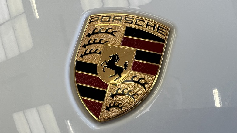 A Porsche emblem, gold with a black horse and name, as well as black antlers and red and black stripes