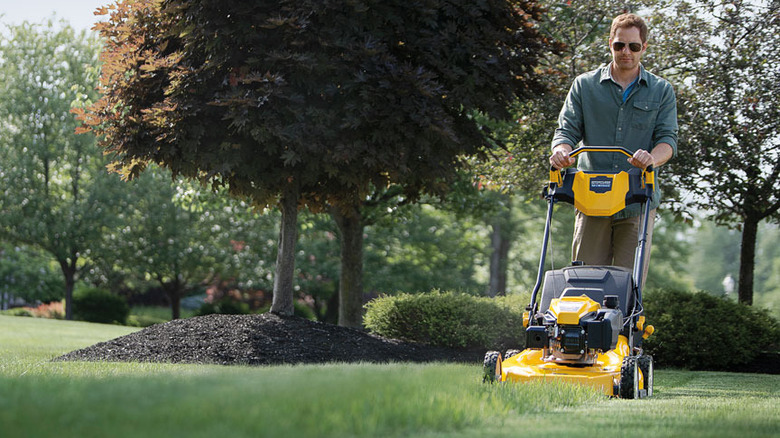 man with sunglases pushing a Cub Cadet gas lawn mower on grass