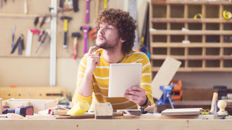 Man in a workshop room holding a paper and in deep thought