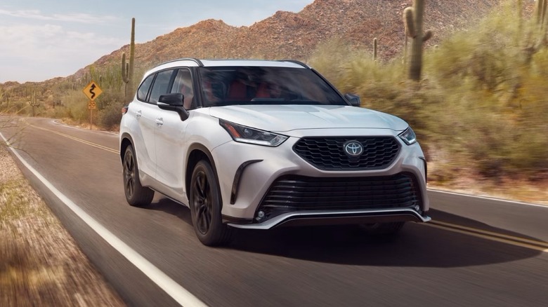 White 2025 Toyota Highlander driving on a road with mountains in the background