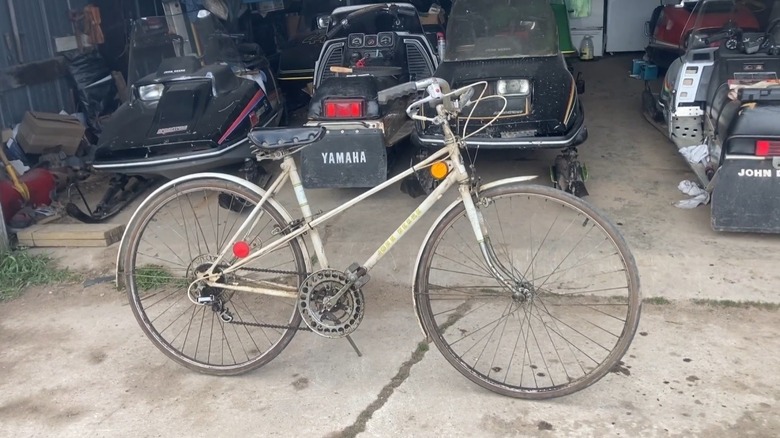 White 1970s woman's John Deere bicycle in front of a row of old snow mobiles.