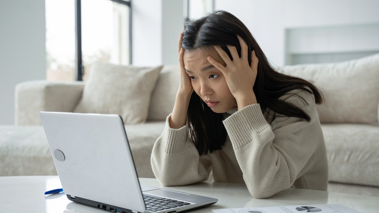 Person with hands on their head looking at a laptop screen